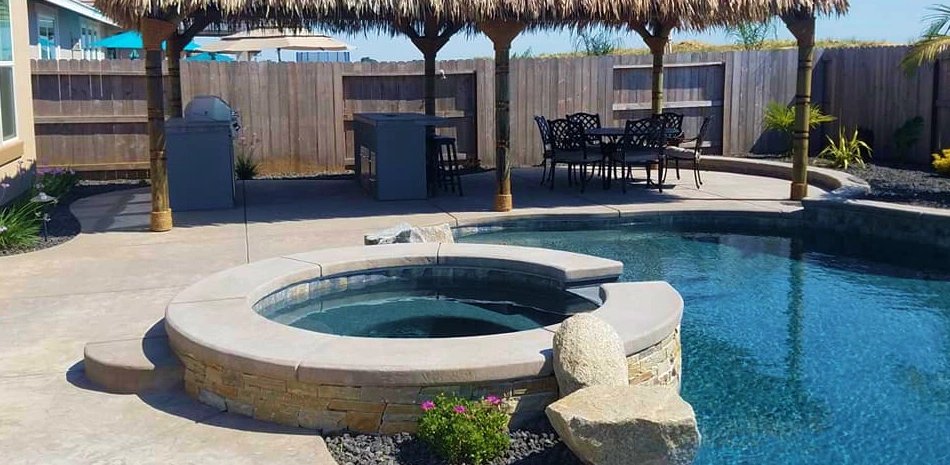 Raised stone spa beside a pool with thatched palapas behind it