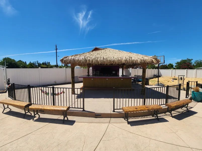 Large palapa bar behind a pool fence with built-in bench seating